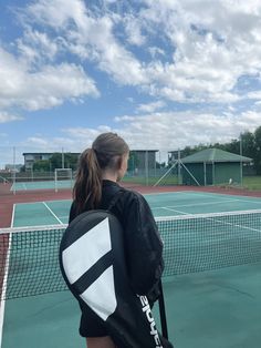 a woman holding a tennis racket on top of a tennis court with clouds in the background