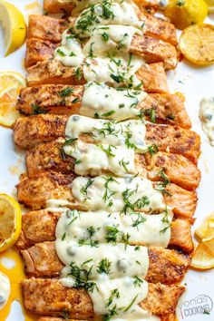 grilled salmon with lemon and dill sauce on a white platter next to sliced lemons