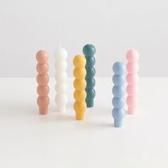 four candles are lined up in different colors and sizes on a white surface, with one candle turned upside down to the side