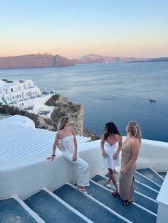 three women standing on the edge of a building looking out at the water and buildings