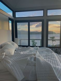 an unmade bed in front of large windows with the ocean out to the side