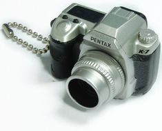 a silver camera with a chain attached to it's body and the lens is open