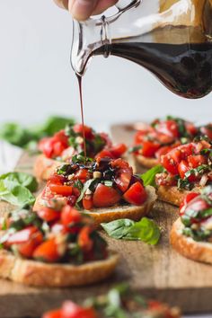 someone is pouring dressing onto small pieces of bread topped with tomatoes and lettuce