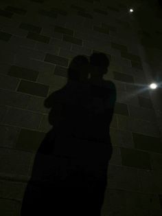 two people standing next to each other in the dark with their shadows on the ground