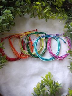 several different colored bracelets sitting on top of a white cloth next to green plants