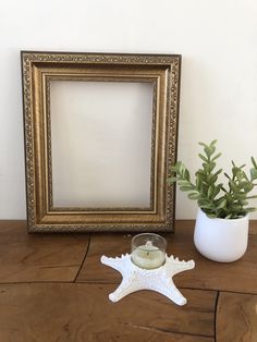 a white starfish candle holder next to a gold frame and potted plant on a wooden table