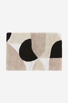 a rug with black, white and beige shapes on the floor in front of a gray wall