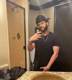 a man taking a selfie in front of a bathroom mirror while wearing a hat