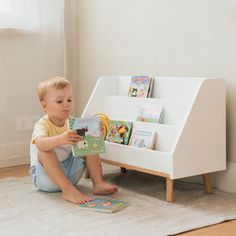 a young boy sitting on the floor reading a book in front of a white children's bookshelf