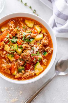 a white bowl filled with meat and vegetable soup next to a spoon on top of a table