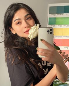 a woman taking a selfie with her cell phone and flower in her mouth,