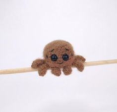 a brown stuffed animal hanging on to a wooden stick with eyes wide open and one eye partially closed