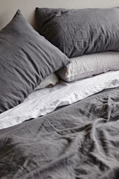 an unmade bed with grey linens and pillows