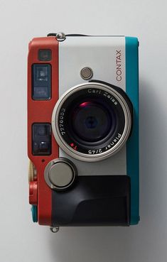 an old camera sitting on top of a white table next to a blue and red case