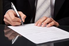 a man in a suit writing on a piece of paper next to a pen and notebook