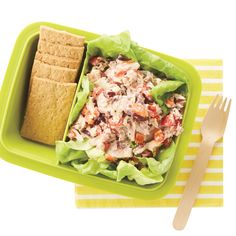 a green container filled with lettuce and chicken salad next to crackers on a yellow striped napkin