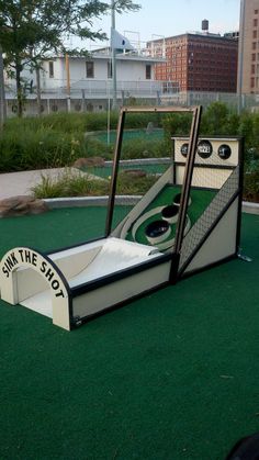 an artificial miniature golf course in the middle of a park with grass and buildings behind it