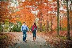 a man and woman holding hands walking down a path in the woods with fall foliage