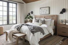 a bedroom with white walls and wood floors, along with a large bed covered in gray and white blankets