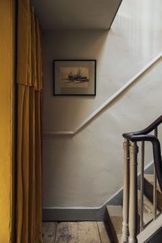 a stair case next to a yellow curtain on the side of a wooden handrail