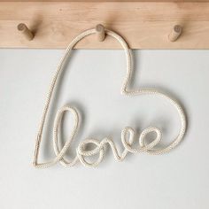 the word love spelled with rope hanging from hooks on a white wall in front of a wooden frame