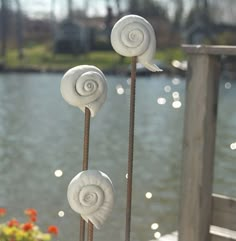 three white snails are standing next to each other on sticks by the water's edge