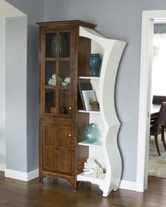 a tall wooden cabinet with glass doors and shelves in the middle of a living room