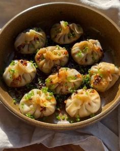 a brown bowl filled with dumplings on top of a white cloth next to a wooden table