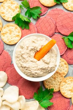 a bowl of dip surrounded by crackers and vegetables