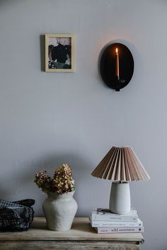 a table with a lamp, vase and pictures on the wall behind it in front of a clock