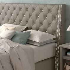 a bed with white headboard and pillows next to a lamp on a nightstand table