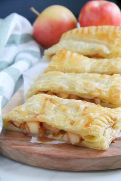 three apple pies sitting on top of a wooden cutting board next to some apples