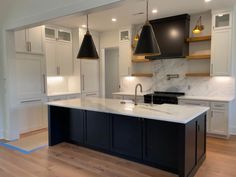 an empty kitchen with black and white cabinets, marble counter tops and wooden flooring