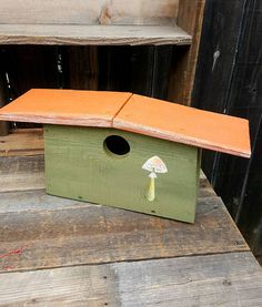 a wooden birdhouse with an orange roof and mushroom stick sticking out of the top