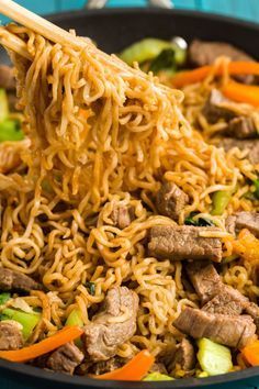 someone is holding chopsticks over noodles with meat and vegetables in a skillet