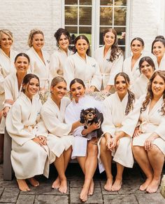 a group of women in white robes posing for a photo with a small black dog