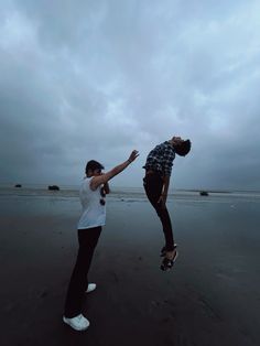 two people on the beach playing with a frisbee in the dark cloudy sky