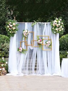 an outdoor wedding setup with white drapes, flowers and gold framed photo frames on the wall