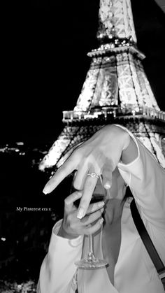 a man holding a wine glass in front of the eiffel tower at night