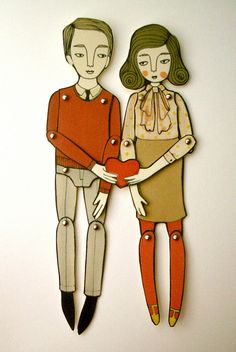 paper cut out of two people standing next to each other on a white surface with one person holding a heart