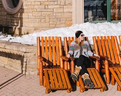 a woman sitting on a wooden chair in front of a building with snow on the ground