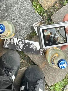 a person holding a camera next to two empty water bottles and an mp3 player on the ground