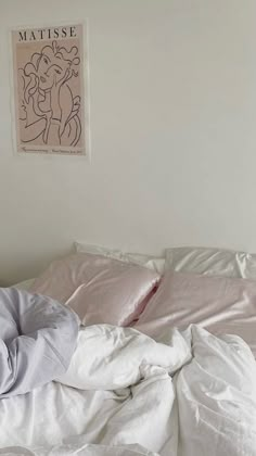 an unmade bed with white sheets and pink comforter next to a poster on the wall