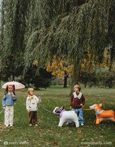 three children with umbrellas are standing in the grass next to toy animals and trees