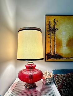 a red lamp sitting on top of a table next to a painting