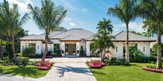 a large white house with palm trees and landscaping on the front lawn, surrounded by lush greenery