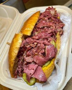 a roast beef sandwich with pickles in a styrofoam container