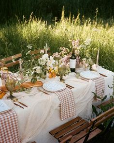 an outdoor table set up with place settings and flowers on it for a dinner party