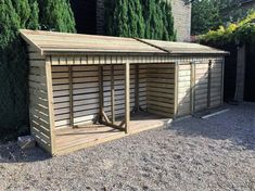 a wooden shed sitting in the middle of a gravel lot next to a tree and shrubbery