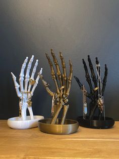 three different types of skeleton hand sculptures on a wooden counter top, one is white and the other is gold